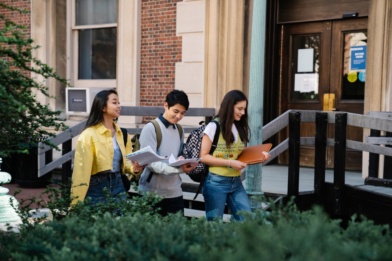 Three college students walking outside on campus, carrying books and smiling. Ideal for educational content.